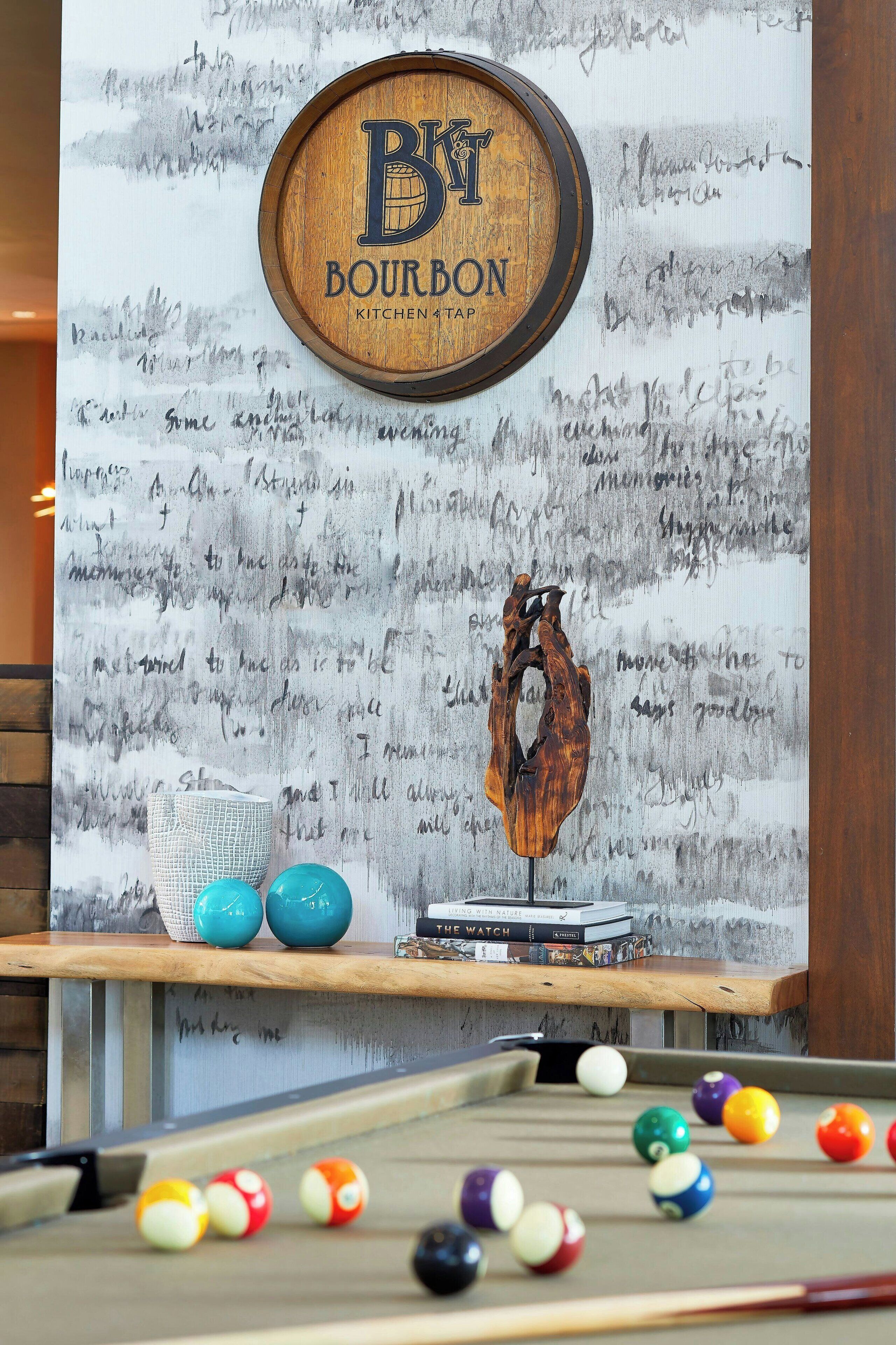 A pool table with balls, a wooden sign with 'Bourbon Kitchen Tap', and a wall with handwritten notes.