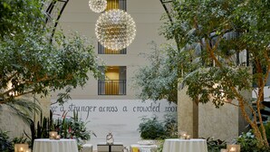 Un giardino interno con tavoli e sedie, un'ampia parete con una citazione e lampade sferiche a sospensione.