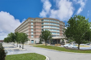A multi-story hotel with a curved facade, parking lot, and surrounding greenery.