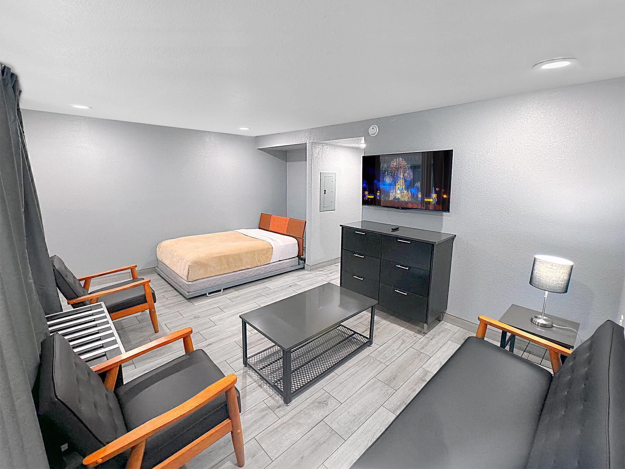 A modern hotel room with a bed, a TV, a desk, and seating area.