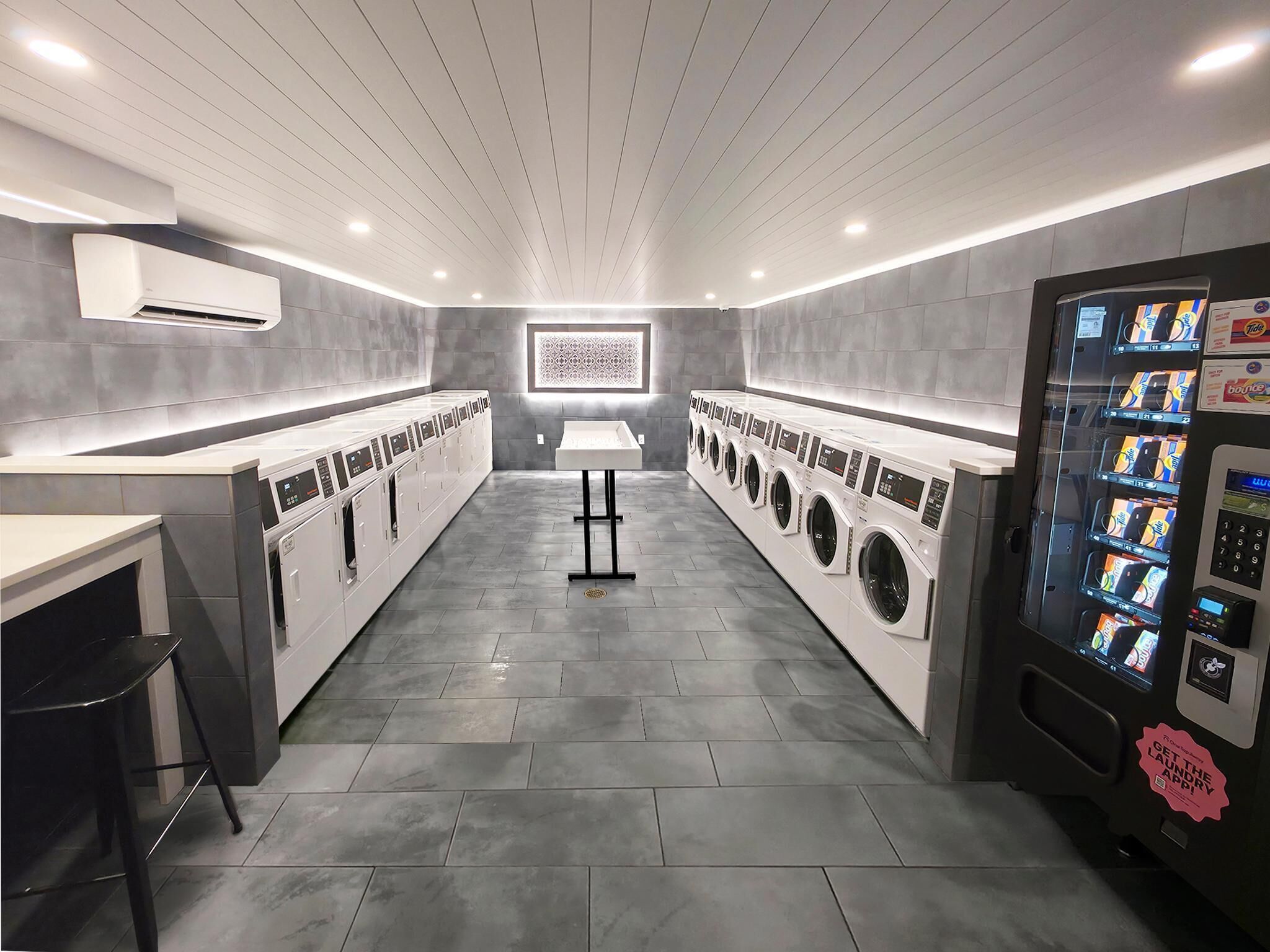 A modern laundry facility with multiple washing machines, a vending machine, and a central table.