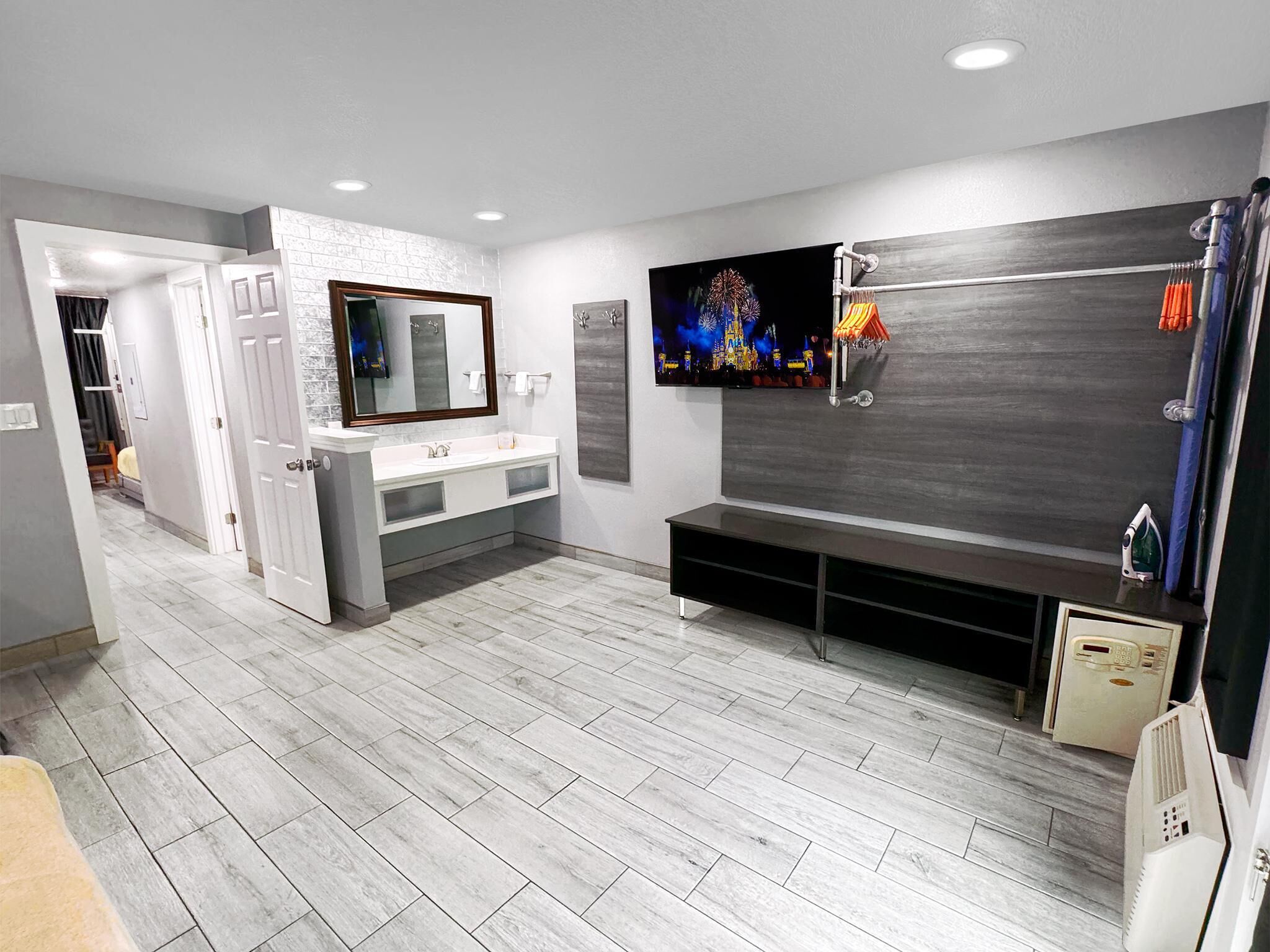 A modern bathroom with a large mirror, a vanity with a sink, a television mounted on the wall, and a shower area.