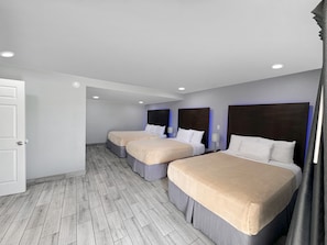 Ein Hotelzimmer mit drei Betten, Holzboden und einer weißen Tür.