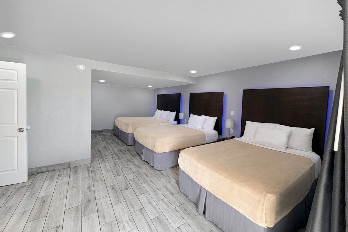 A hotel room with three beds, a wooden floor, and a white door.