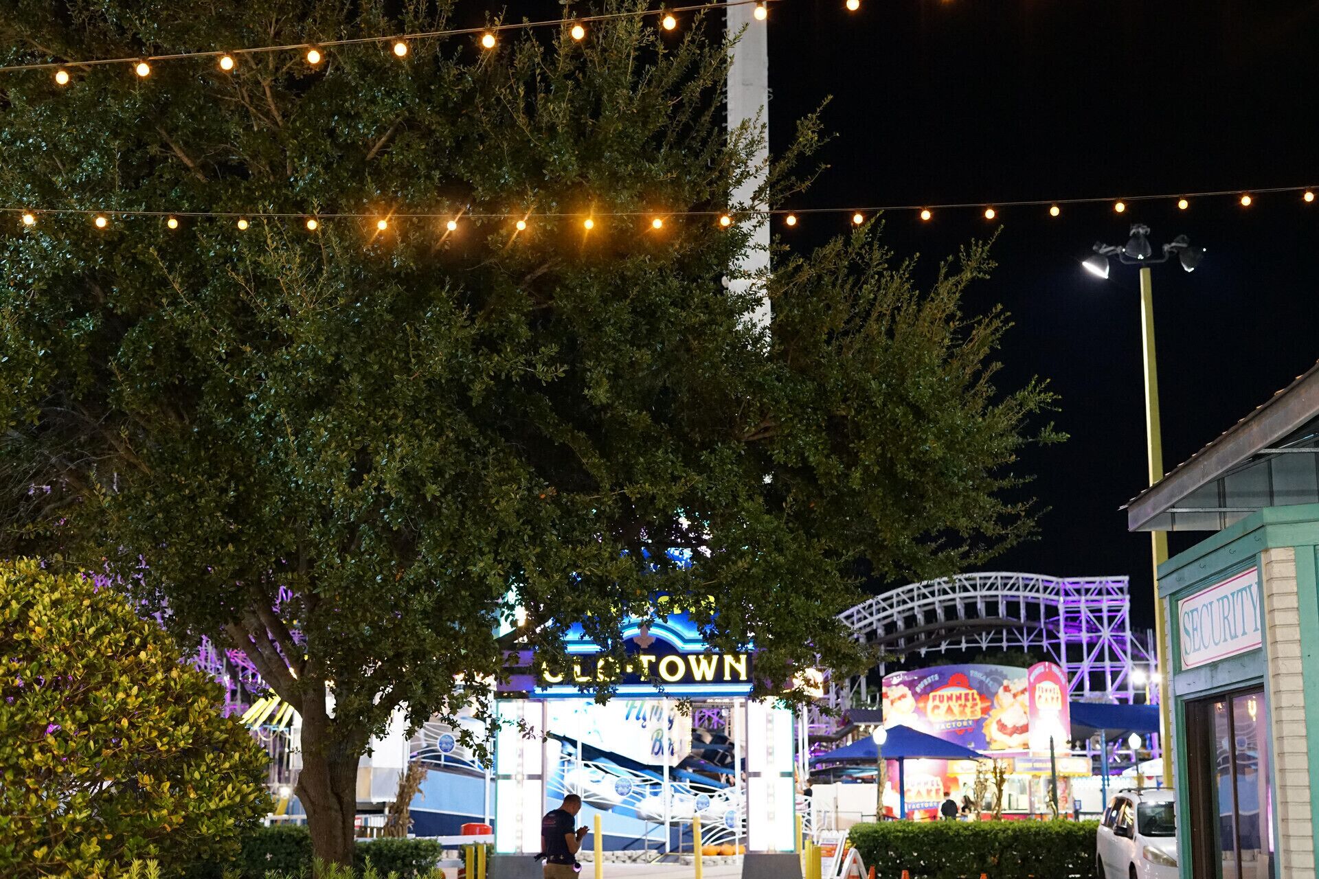 A nighttime view of a themed area with a prominent sign reading 'Funtown' and a roller coaster structure in the background.