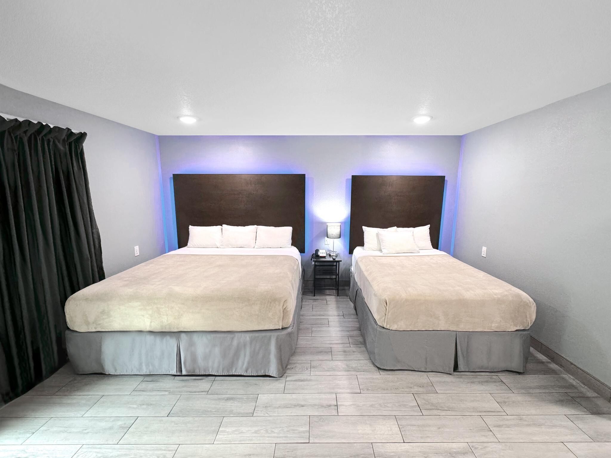 A hotel room with two beds, a nightstand, and a lamp.