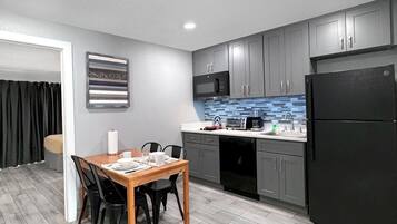 A modern kitchen with grey cabinets, a black refrigerator, and a dining area with a wooden table and chairs.