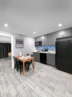 A modern kitchen with grey cabinets, a black refrigerator, and a dining area with a wooden table and chairs. - Celebration Suites (Kissimmee)