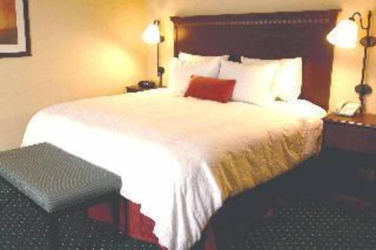 A neatly made bed with pillows, a bedside lamp, and a bench.