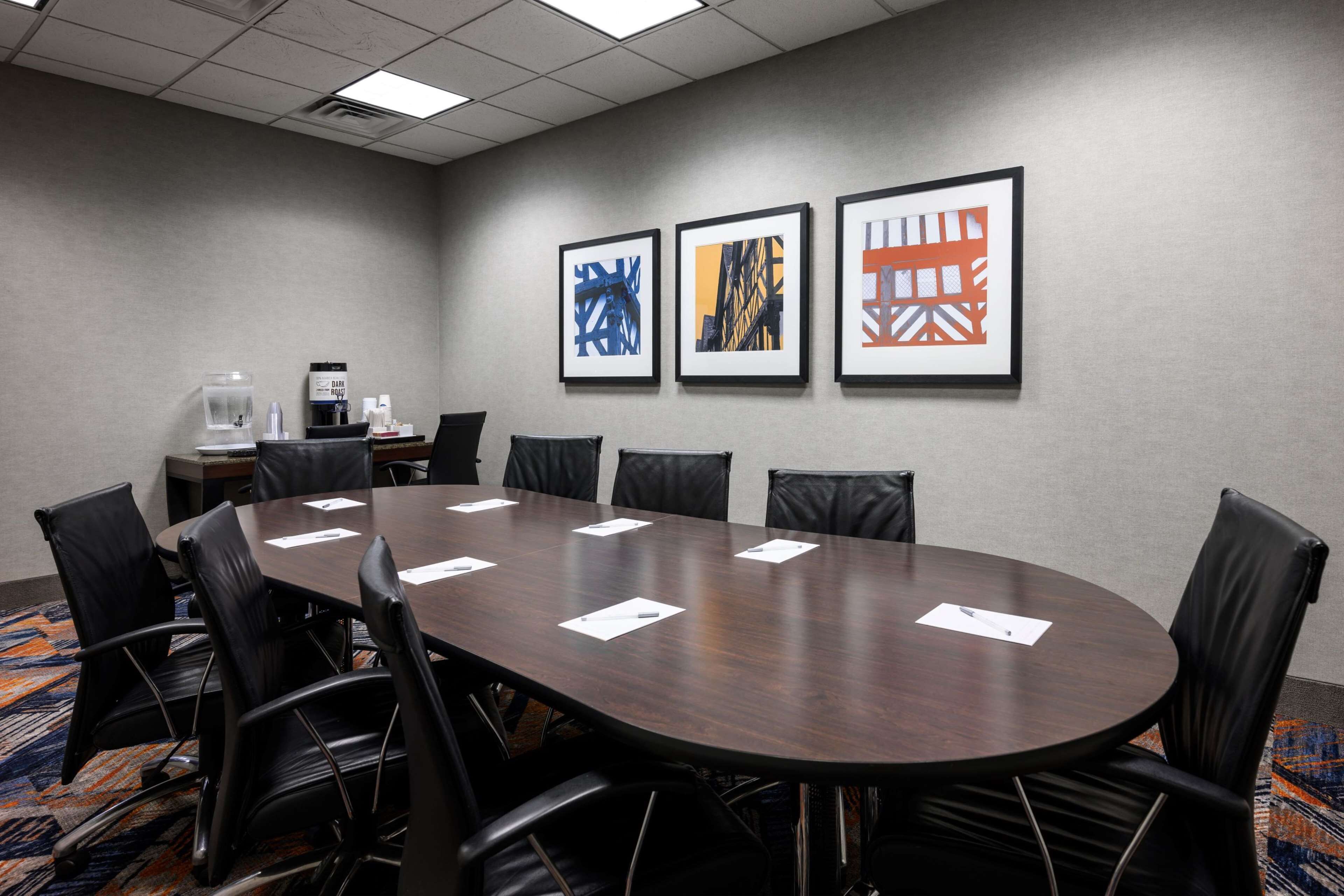 A conference room with a long table, black leather chairs, and framed artwork on the wall.