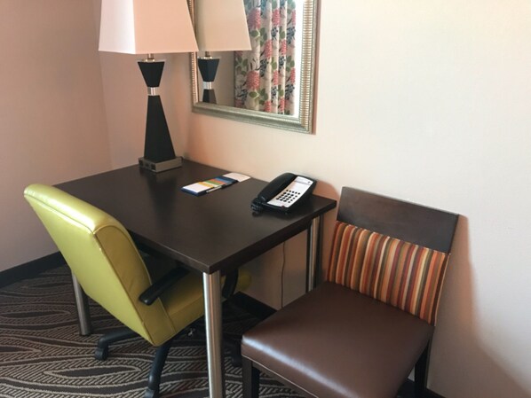 A hotel room with a desk, a telephone, a lamp, a chair, and a striped cushion.