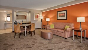 Habitación de hotel con comedor, sofá, dos lámparas y alfombra estampada.