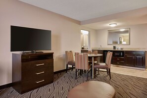A hotel room with a TV, a dining table with chairs, a kitchen area, and a large mirror. - Hampton Inn Evansville/Airport (Evansville)