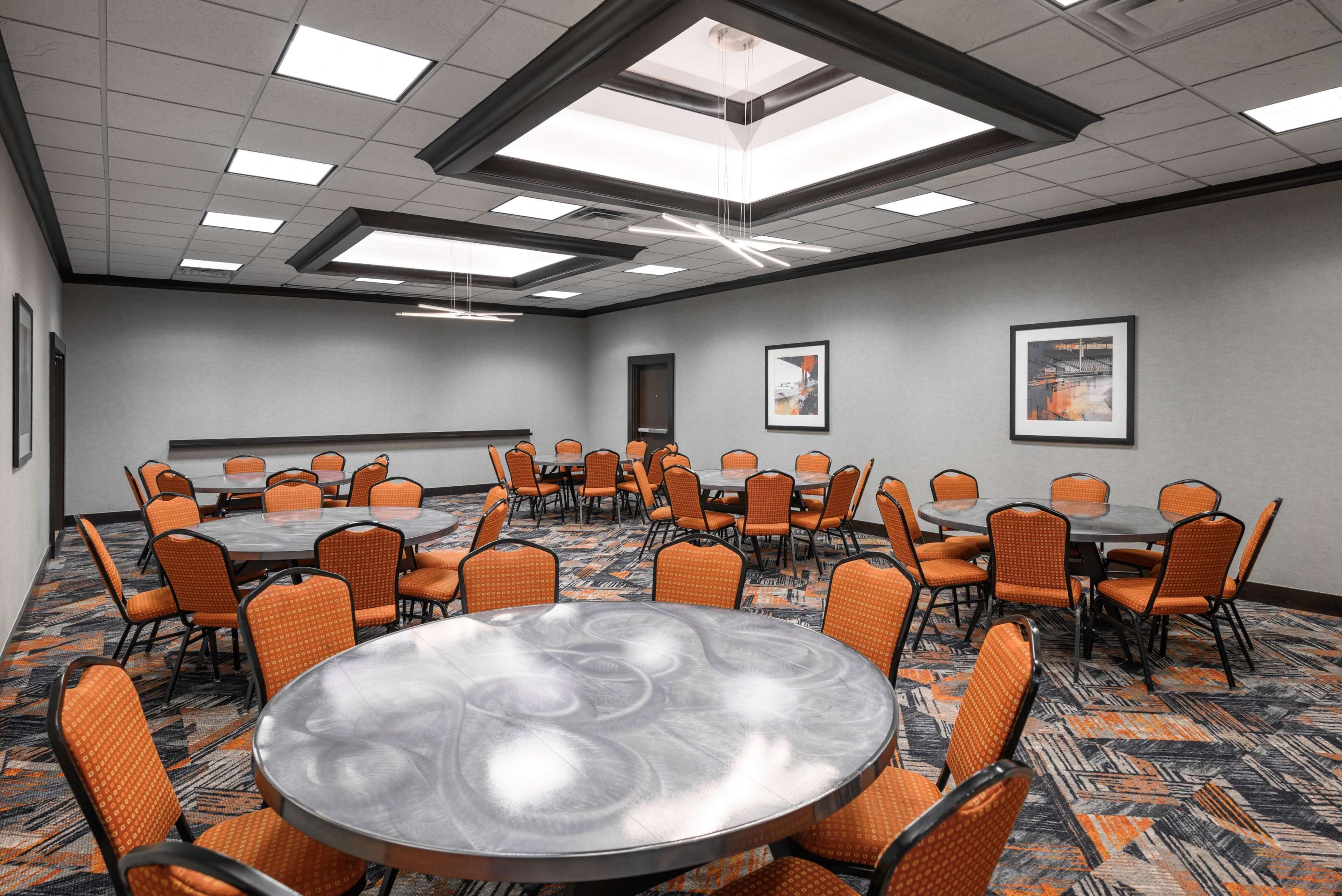 Un salón de conferencias con mesas redondas y sillas naranja, alfombra estampada e iluminación en el techo.