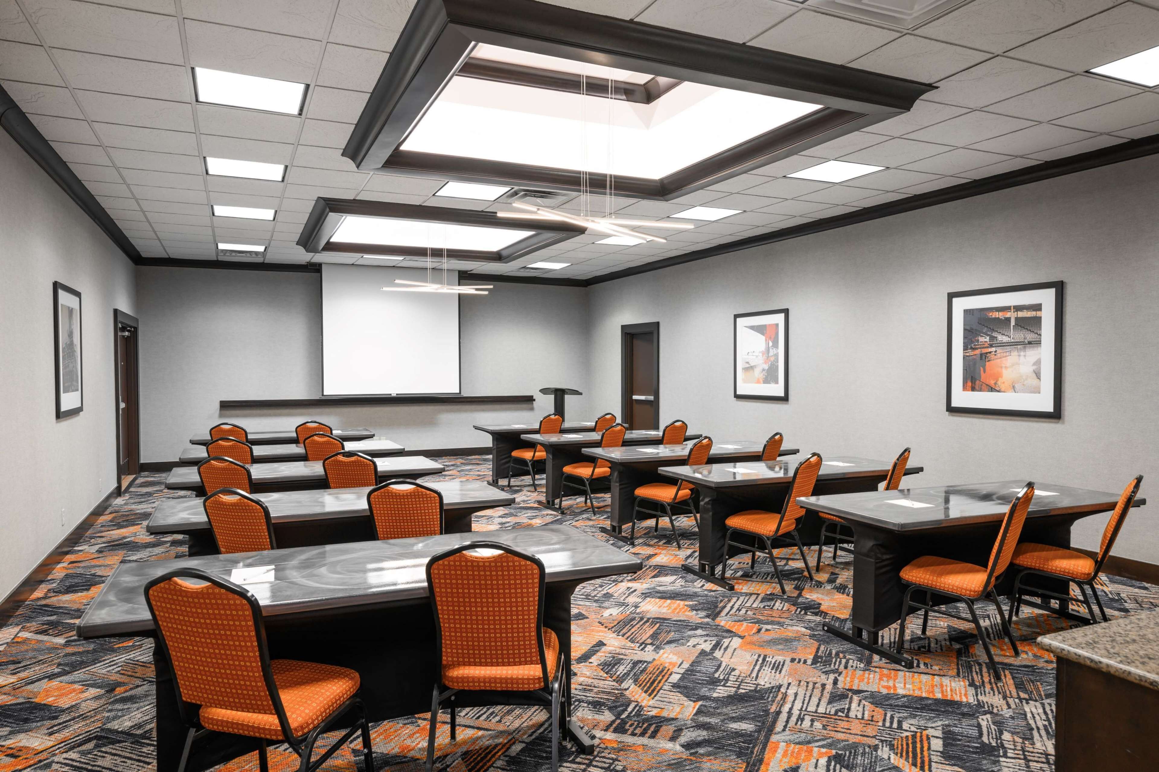 A conference room with multiple tables and chairs, a patterned carpet, and framed pictures on the walls.
