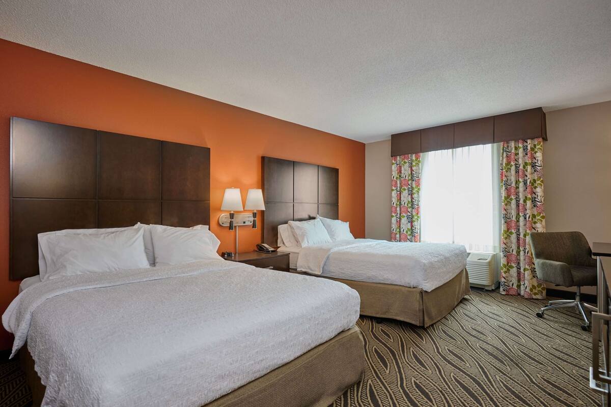 A hotel room with two beds, a desk, a chair, and a window with curtains.