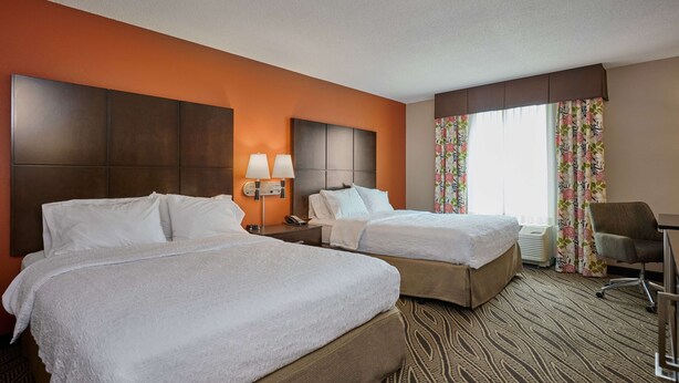 A hotel room with two beds, a desk, a chair, and a window with curtains.