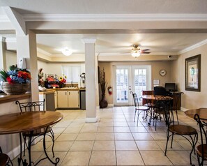 A spacious dining area with a kitchen in the background, featuring a large window and a ceiling fan.