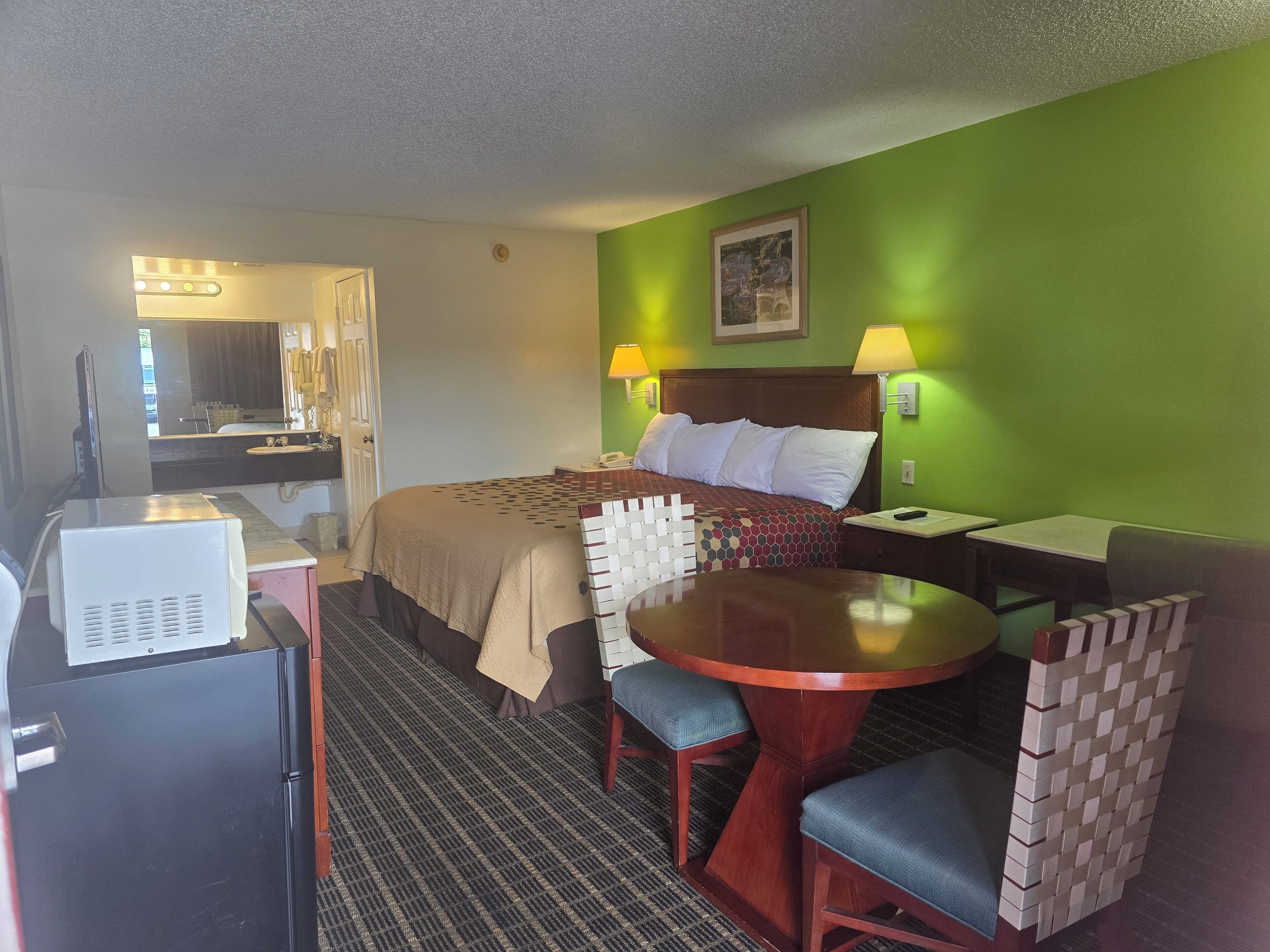 A hotel room with a bed, a desk, a chair, a table, and a mirror.