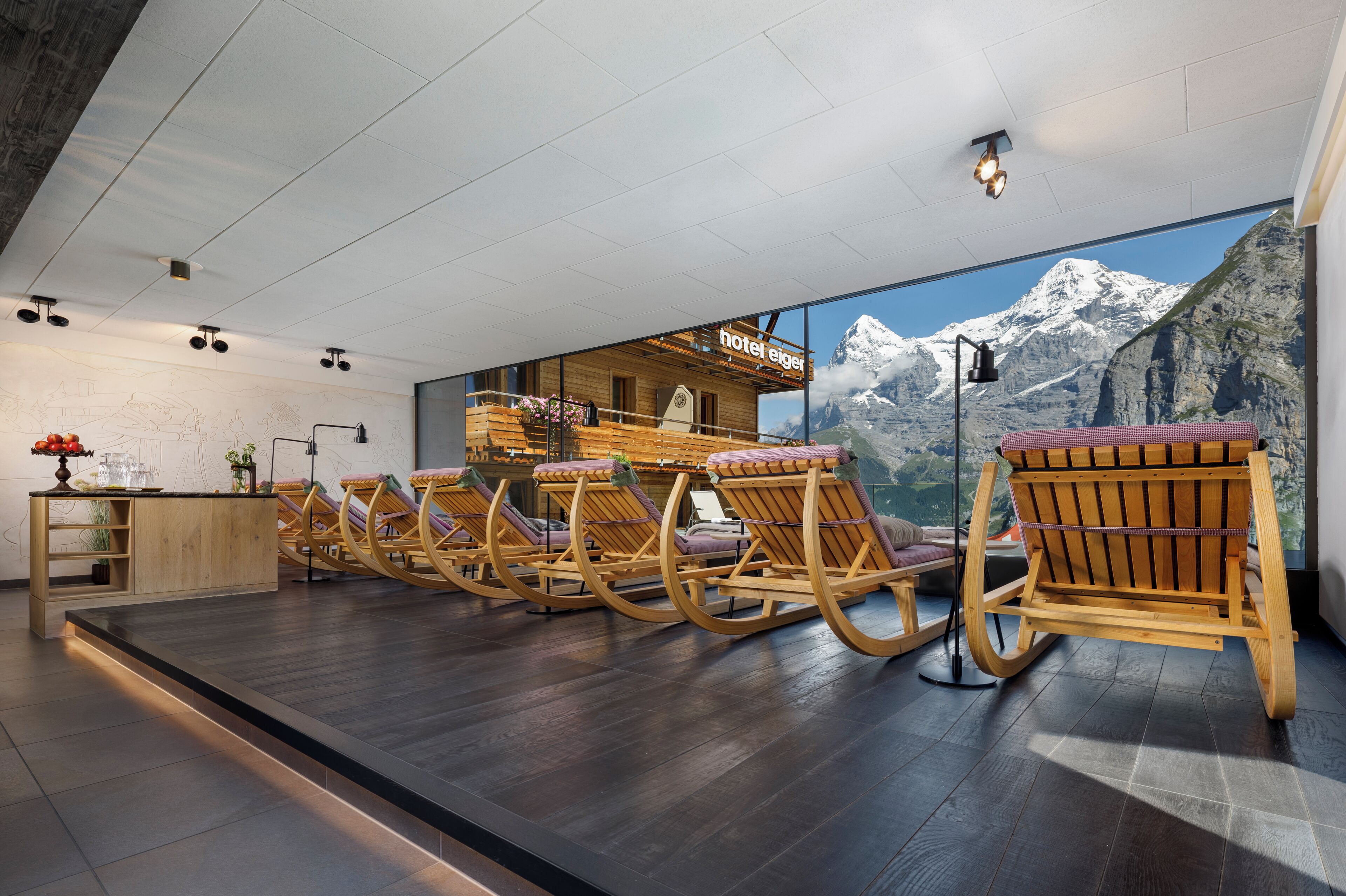 Eine Hotelhalle mit Holzschaukelstühlen, einem Empfangstresen und einem großen Fenster mit Blick auf die Berge.