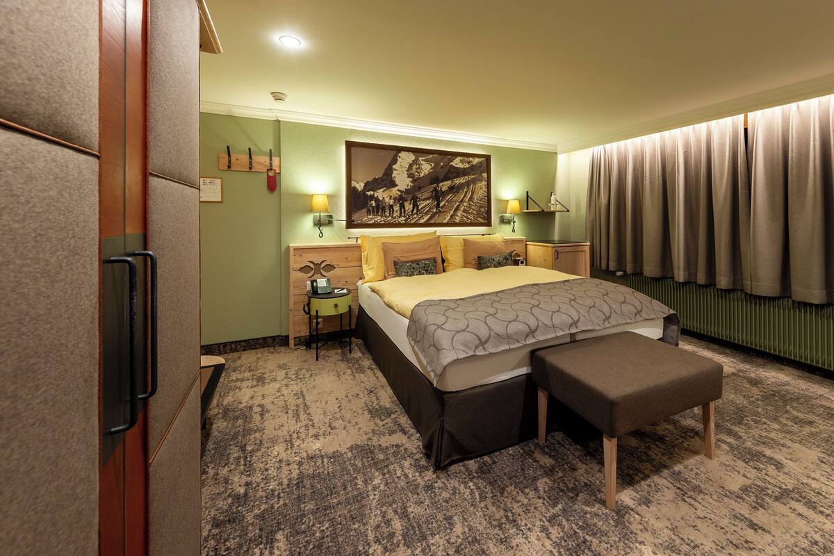 Een hotelkamer met een bed, nachtkastjes, een bankje, een schilderij en gordijnen.