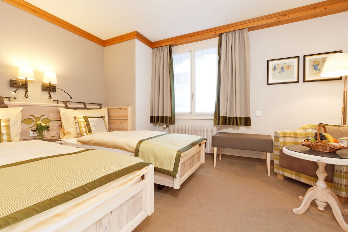 Two single beds with matching headboards, a wooden bench, and a small table are featured in this traditional room.