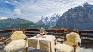 A table set with a bottle, glasses, and a plate of food, overlooking a mountainous landscape. - Eiger Mürren Swiss Quality Hotel (Mürren)