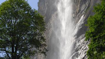 A waterfall cascading down a steep cliff, surrounded by lush greenery and a wooden viewing platform.