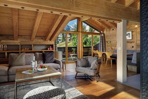 Amplia sala de estar con techos altos, vigas de madera, un sofá, una mesa de centro y vistas al exterior.