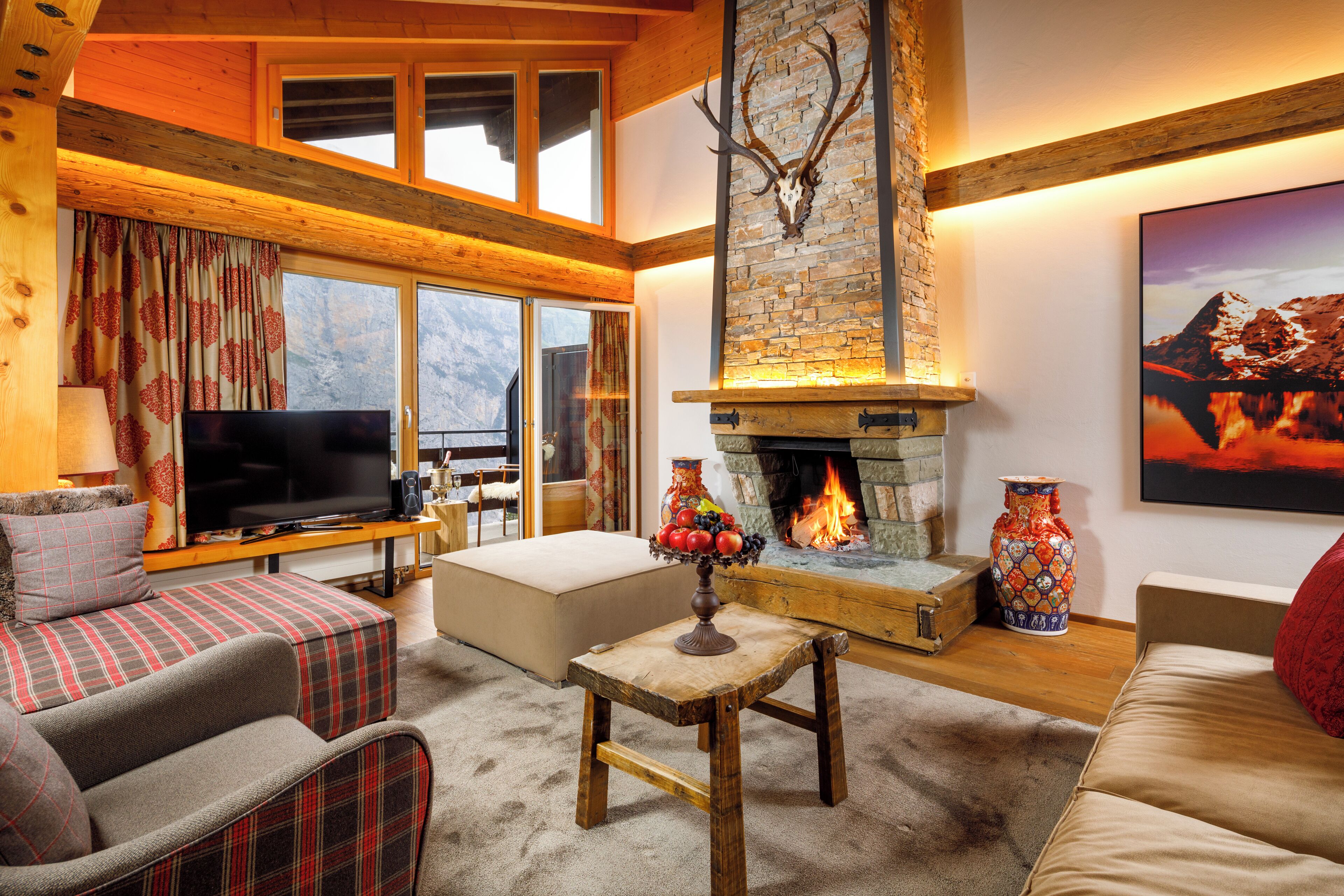 A cozy living room with a fireplace, a television, and a large window overlooking a mountainous landscape.