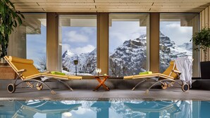 A pool area with two sun loungers, a table, and a view of snow-capped mountains. - Eiger Mürren Swiss Quality Hotel (Mürren)