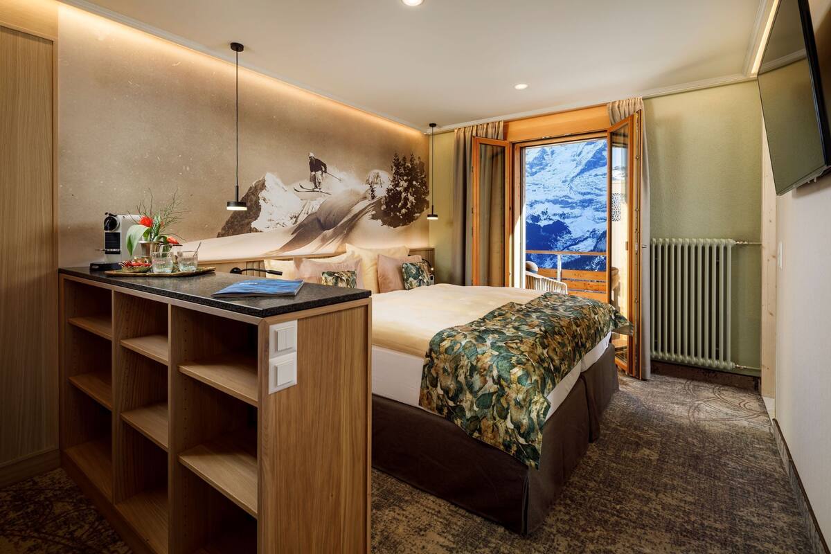 Hotelkamer met een bed, een bureau met een computer, een radiator en een raam met uitzicht op bergen.