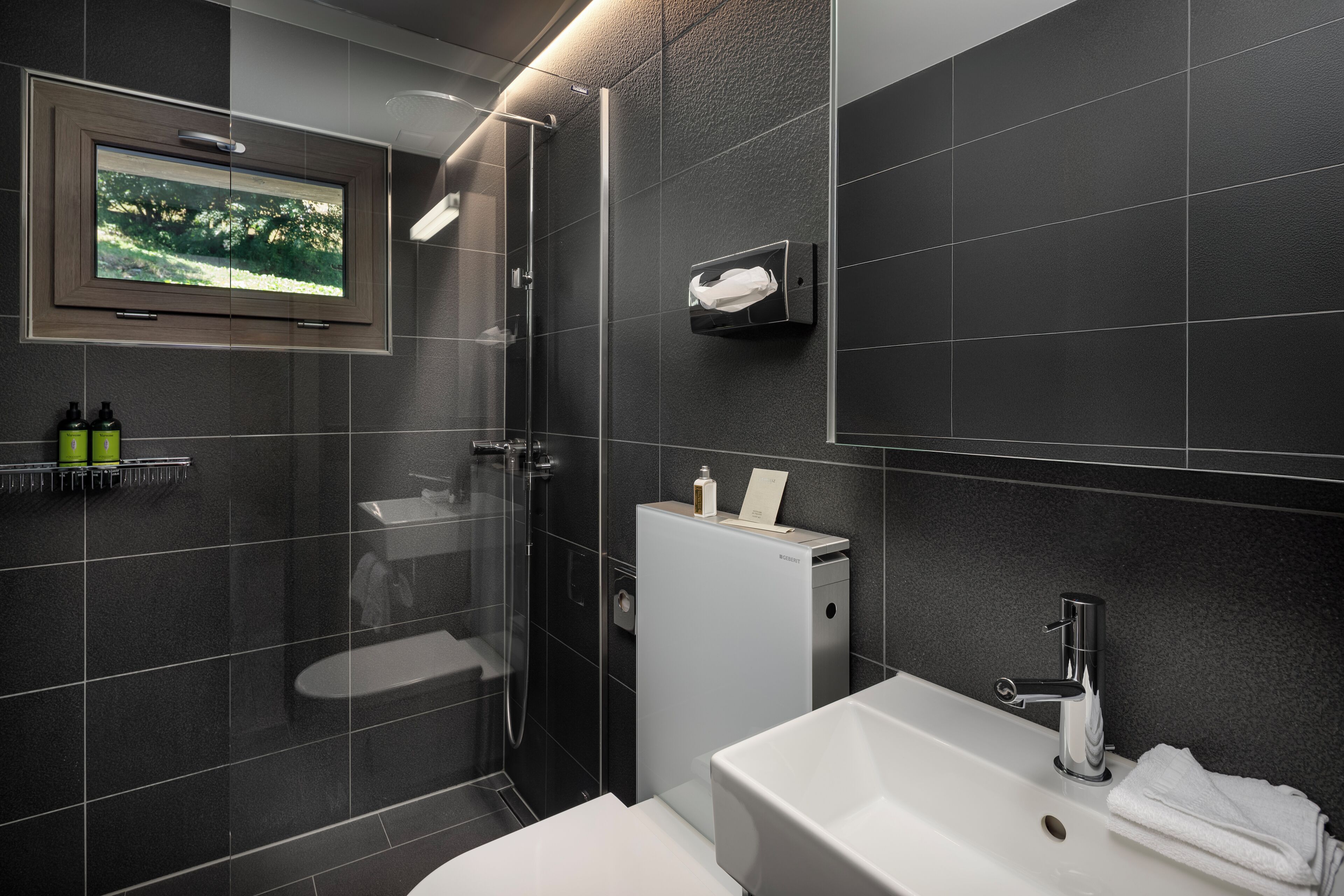 Une salle de bain moderne équipée d’une douche, de toilettes, d’un lavabo et d’un téléviseur fixé au mur.