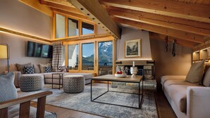 A cozy living room with a wooden ceiling, a sofa set, a coffee table, and a view of mountains through large windows. - Eiger Mürren Swiss Quality Hotel (Mürren)