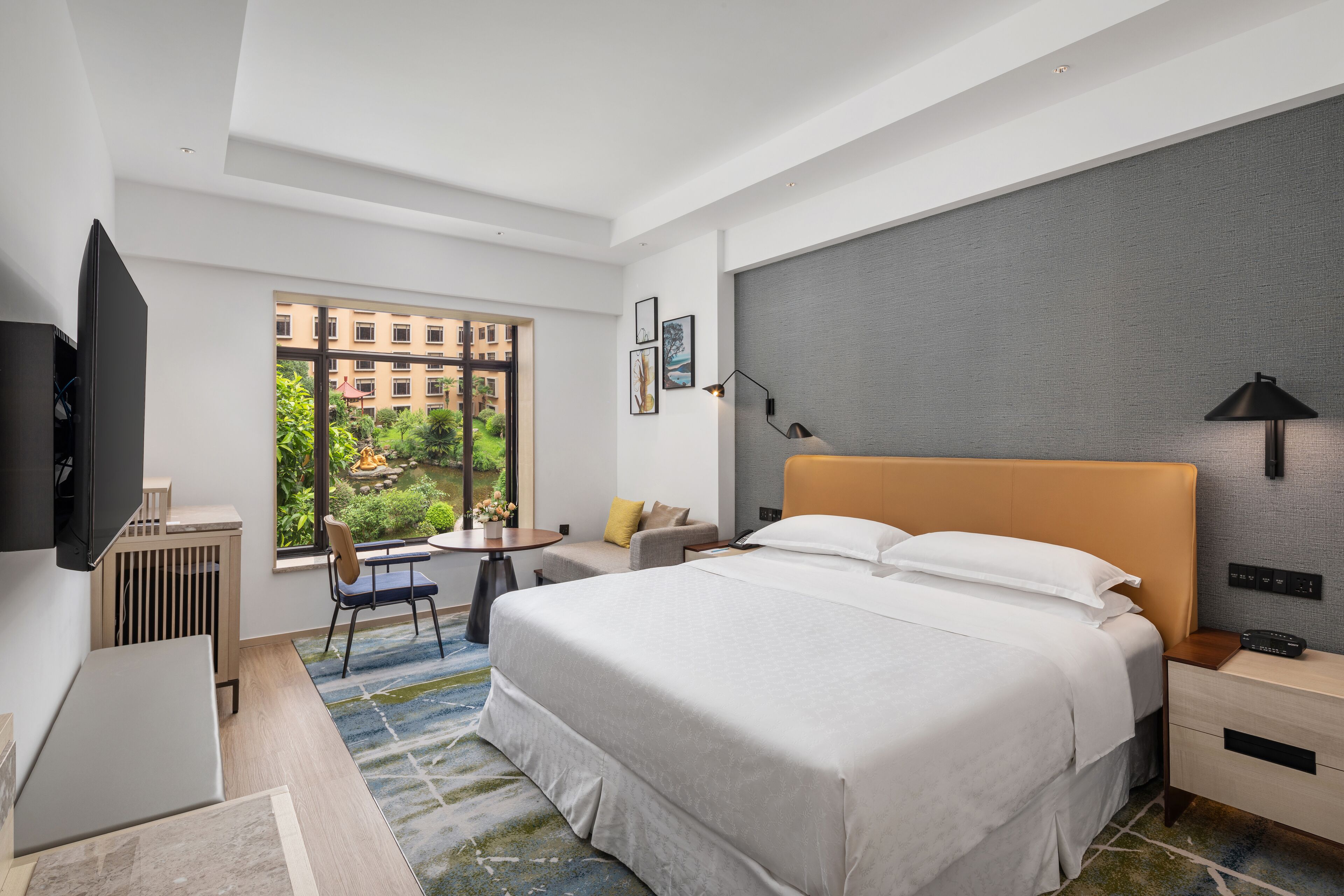 Ein modernes Hotelzimmer mit einem großen Bett, einem Schreibtisch, einem Stuhl, einem kleinen Tisch und einem Fernseher.