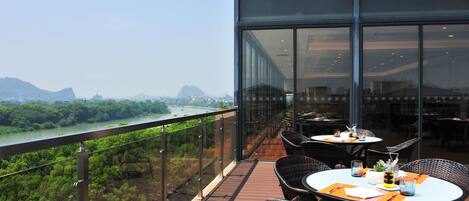 A restaurant with outdoor seating overlooking a river and mountains.