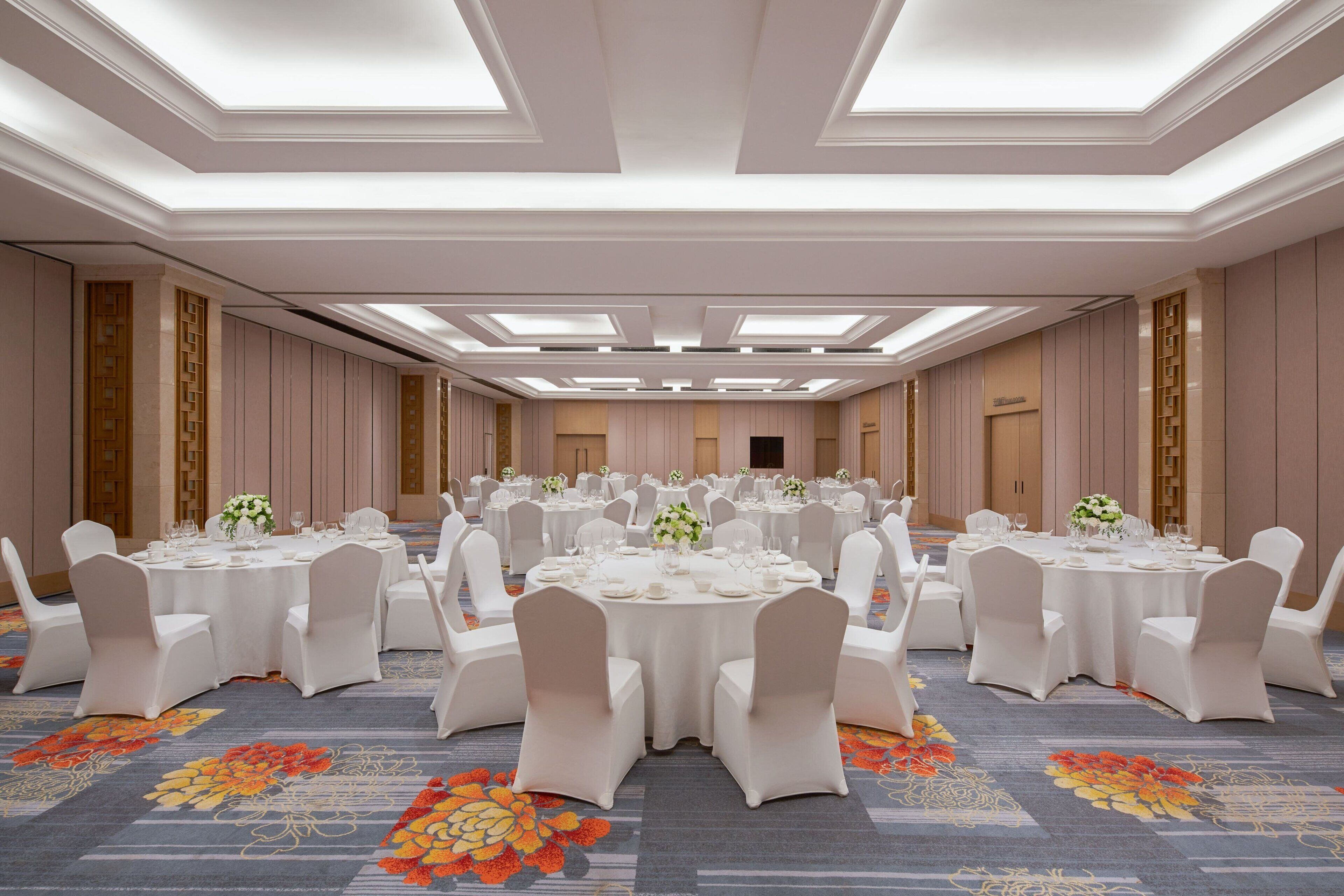 A banquet hall with round tables, white chairs, and floral centerpieces.