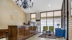 A hotel lobby with a reception desk, a chandelier, a green armchair, a blue sofa, and large windows. - Quality Inn San Angelo (San Angelo)