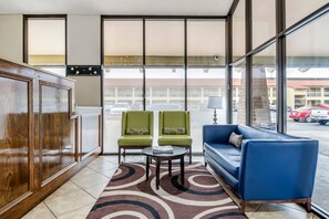 A hotel lobby with a wooden cabinet, two green armchairs, a blue sofa, a small table, and large windows offering a view of the parking lot. - Quality Inn San Angelo (San Angelo)