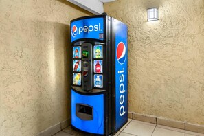 A Pepsi vending machine in a corner with a textured wall and a small window. - Quality Inn San Angelo (San Angelo)
