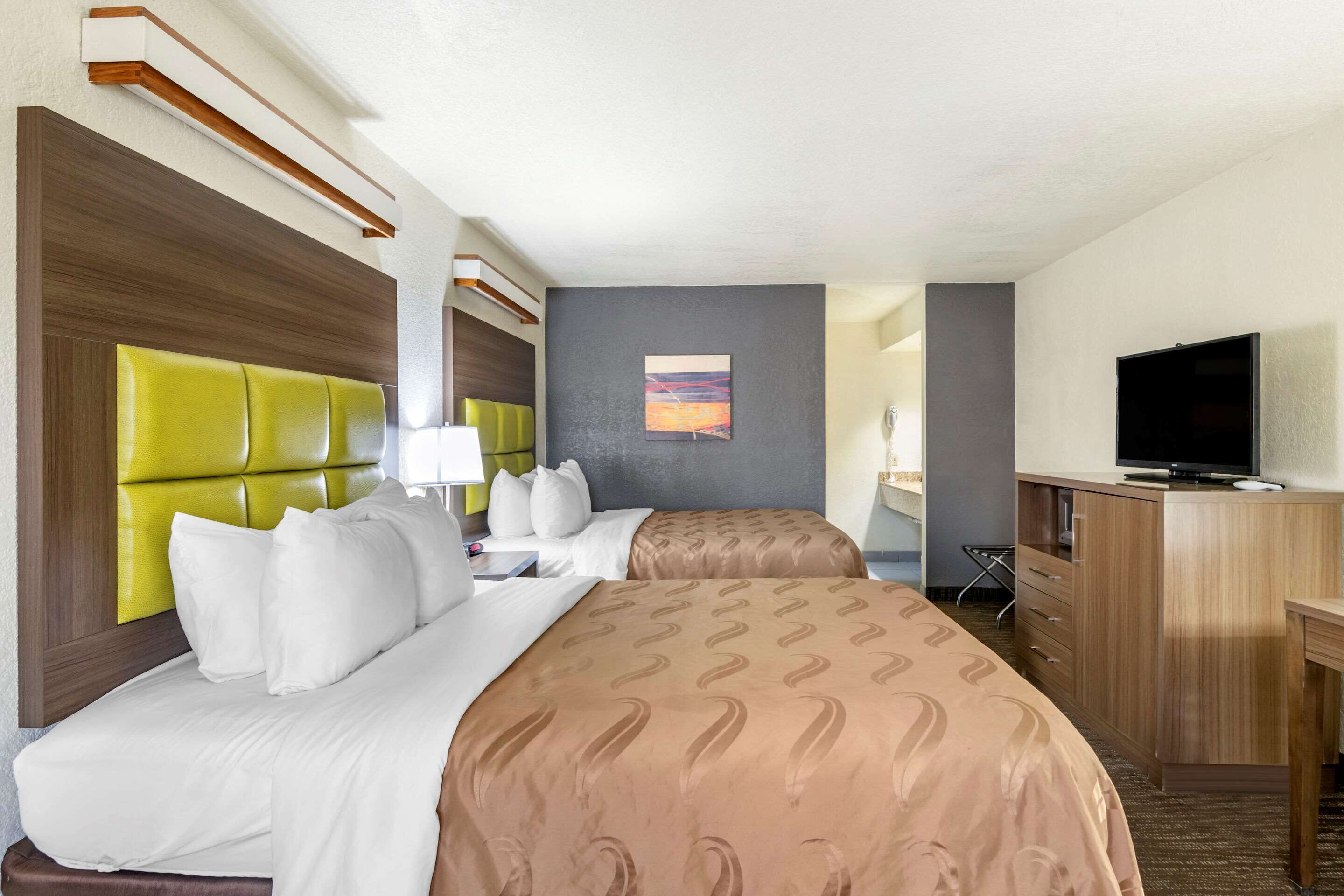 A hotel room with two beds, a television, a desk, and a painting on the wall.