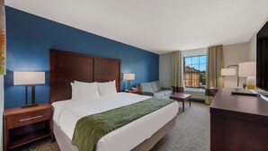 Een hotelkamer met een groot bed, een bureau, een stoel en een bank. Er is een raam met uitzicht op gebouwen.