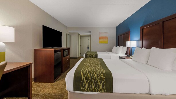 Een hotelkamer met een groot bed, een bureau met een televisie, een dressoir en een schilderij aan de muur.