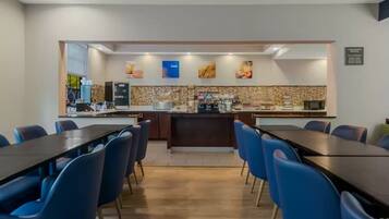 A modern hotel dining area with a central bar, blue chairs, and a tiled backsplash.