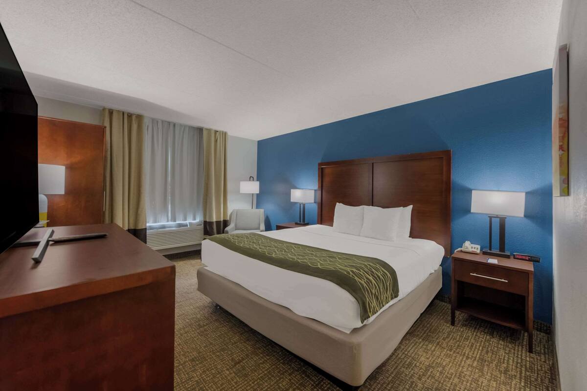 Une chambre d’hôtel avec un grand lit, deux tables de chevet avec des lampes, un bureau avec une télévision et une fenêtre avec des rideaux.