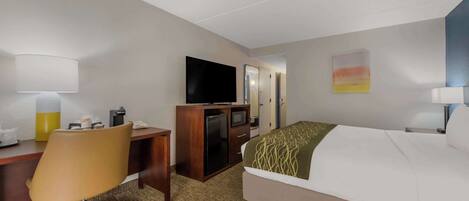 A hotel room with a bed, a desk with a chair, a television, a refrigerator, and a small cabinet.