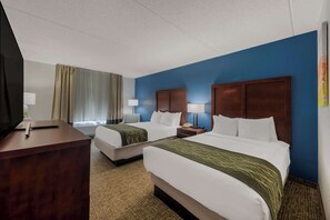 A hotel room with two beds, a desk, a TV, and a window with curtains.