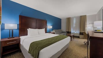 Habitación de hotel con una cama grande, un escritorio, una silla, una mesita de noche y una lámpara.