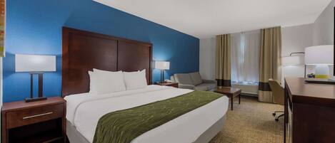 A hotel room with a large bed, a desk, a chair, a nightstand, and a lamp.