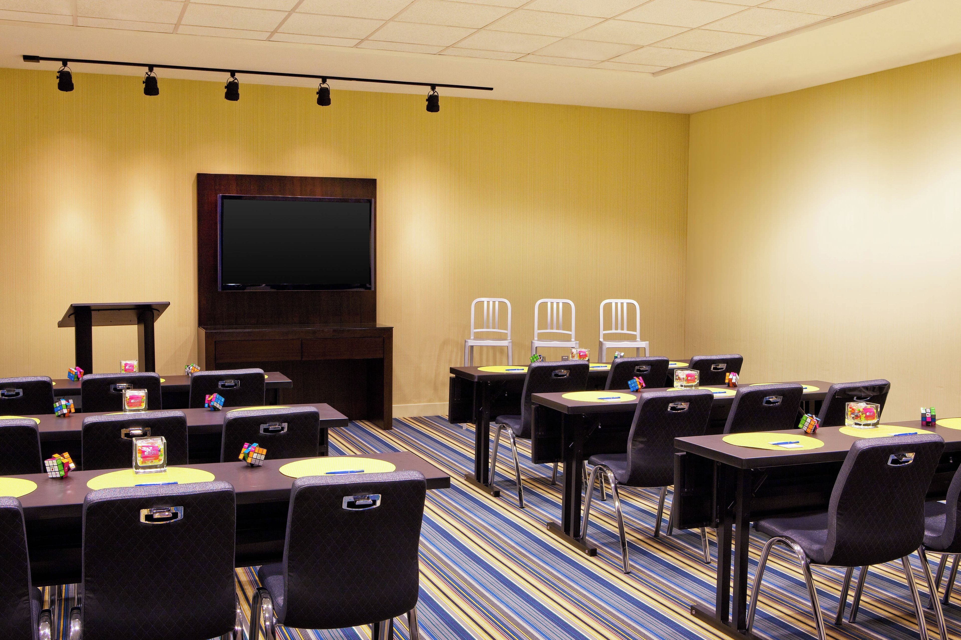 Un salón de conferencias con mesas, sillas, un atril y una pantalla grande.